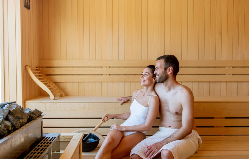 Mann und Frau entspannen in einer Holzsauna, beide in Handtücher gehüllt, in den Appartements Sellraintail.