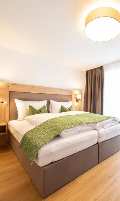 Ein modernes Zimmer im Appartment Sellrain mit einem Doppelbett, grünen Akzenten und natürlichem Fensterlicht.